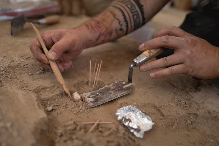 A fragment of red ochre pigment is excavated by an archaeologist. One of the most common finds at the site, red ochre may have been used to decorate the floors of dwellings, or for some other unknown purpose. 